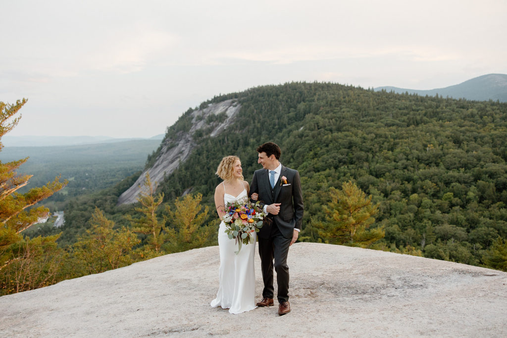 Summer elopement in New Hampshire - bride and groom walking arm in arm with epic views. 
