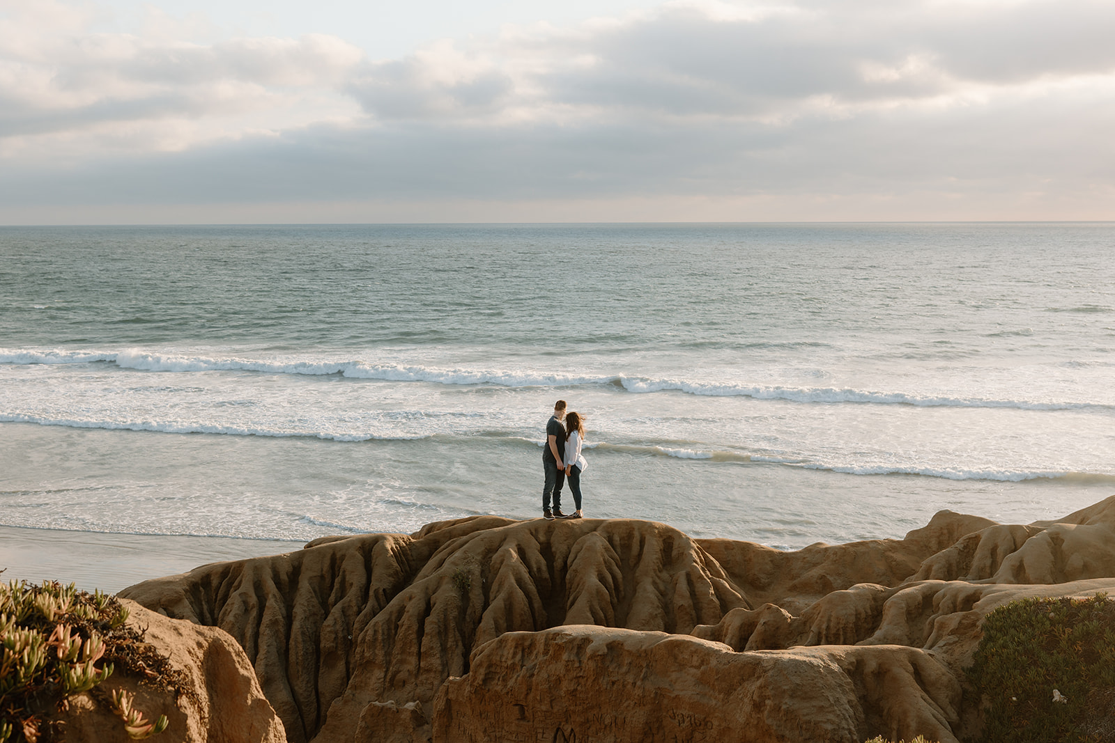Engaged couple embracing on Carlsbad cliffs