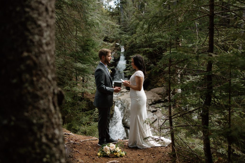 Bride and groom reading vows at waterfall in New Hampshire